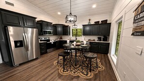 A kitchen with dark cabinets, stainless steel appliances, a round dining table with stools, and a decorative rug. - Romantic Retreat with Hot Tub & Fire Pit in Broken Bow, Oklahoma (Broken Bow)