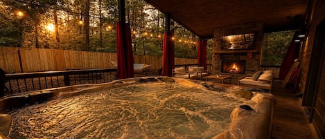 Un bain à remous avec une cheminée en pierre, une terrasse en bois et des guirlandes lumineuses.