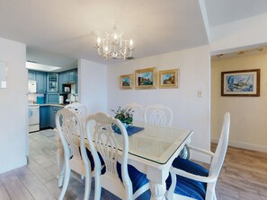 A dining area with a table, chairs, and a chandelier. There are framed pictures on the wall. - Wake Up to Ocean Views | Castle Reef 411 (New Smyrna Beach)