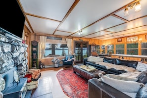 Ein gemütliches Interieur mit Kamin, einer Ledersofa, einem roten Teppich und Blick ins Freie.