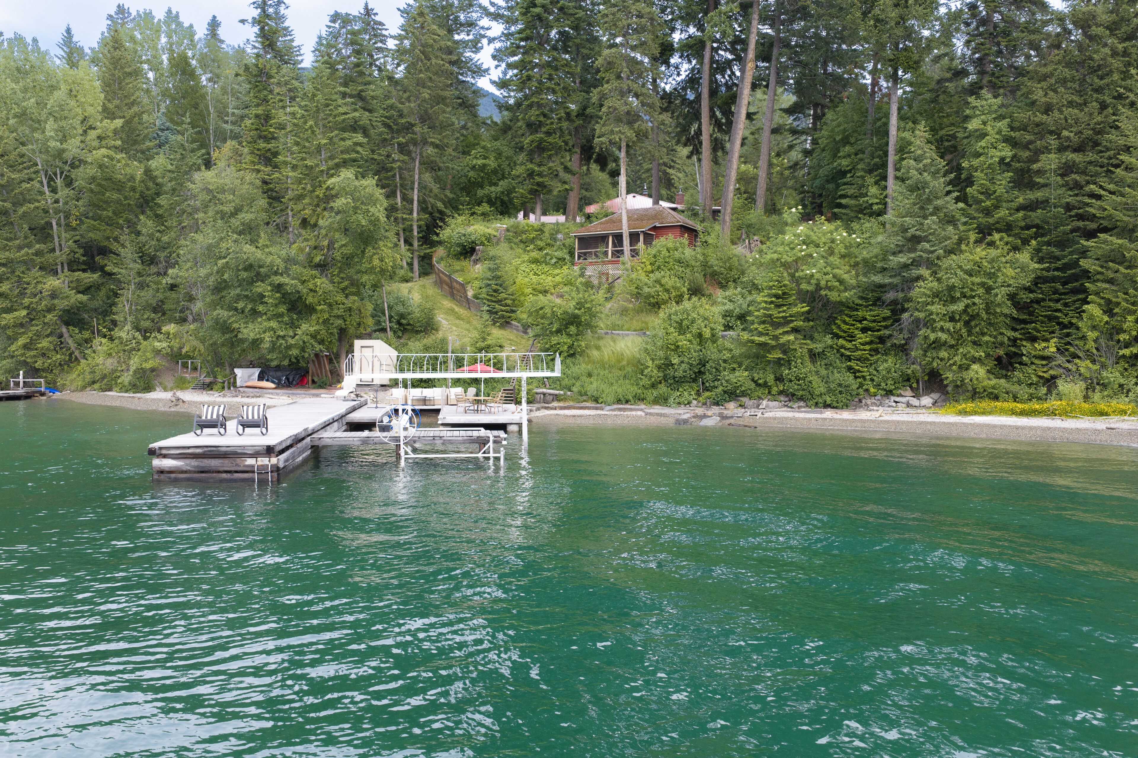 A dock with chairs, a boat, and a house surrounded by dense forest.