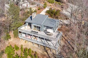 Une maison à deux étages dotée d’une terrasse, entourée d’arbres et d’un paysage rocheux.