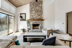 Un salon moderne avec une cheminée en pierre, de grandes fenêtres et un coin salon confortable.