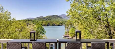 A balcony with wicker chairs and two lanterns overlooking a lake surrounded by trees and hills.