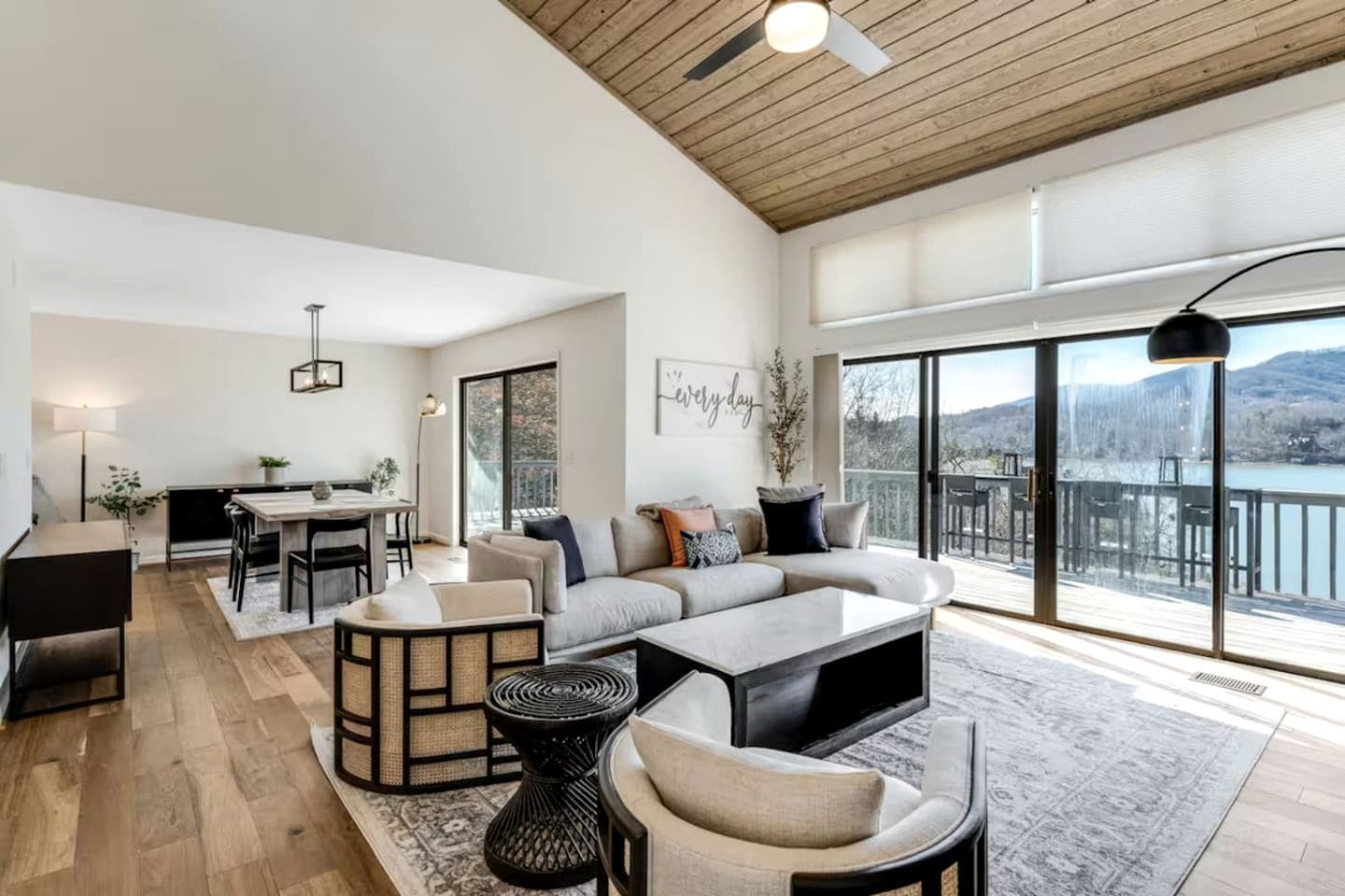 A spacious living area with a large sofa, a dining table, and a balcony with a view of the mountains.