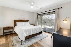 Ein Schlafzimmer mit einem Bett, Nachttischen, einem Schreibtisch, einem Sessel, einer Schreibtischlampe und Blick durch eine Schiebetür.