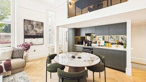 A modern kitchen with dark cabinets, a marble island, and a dining area with a round table and four chairs. - Decadent and Exquisite Holland Park Duplex (Greater London)