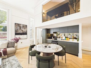 A modern kitchen with dark cabinets, a marble island, and a dining area with a round table and four chairs. - Decadent and Exquisite Holland Park Duplex (Greater London)
