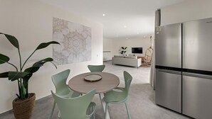 A modern kitchen with a stainless steel refrigerator, a dining area with a round table and chairs, and a living area with a sofa and TV. - Apartement Isla Mambo Beach  (Willemstad)