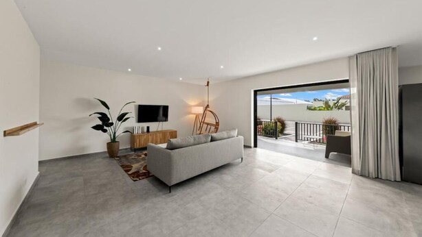 A modern living room with a sofa, a TV, a plant, and a view to the outside. - Apartement Isla Mambo Beach  (Willemstad)