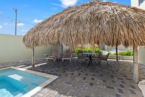 Ein Poolbereich mit einem Reetdach, Liegestühlen und einer gefliesten Terrasse.
