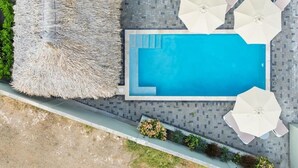 An aerial view of a swimming pool with a tiled deck, surrounded by white umbrellas and a thatched lounge area. - Apartement Isla Mambo Beach  (Willemstad)