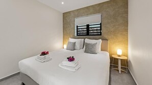 A modern bedroom with a large bed, bedside lamps, and a wall-mounted mirror. - Apartement Isla Mambo Beach  (Willemstad)
