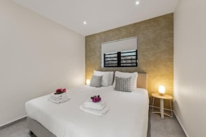 Ein modernes Schlafzimmer mit einem großen Bett, Nachttischlampen und einem Wandspiegel.