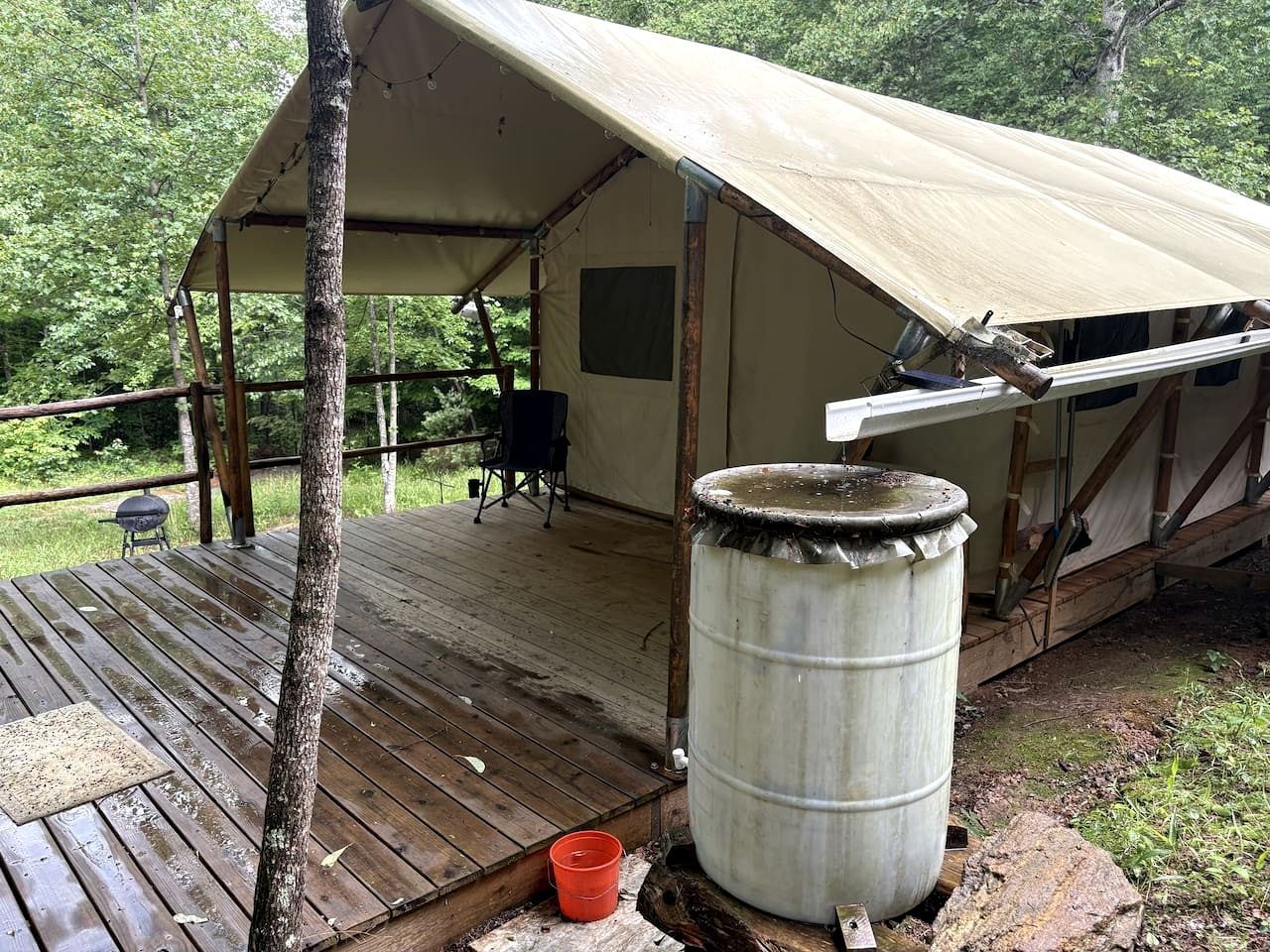 A tent with a wooden deck, a metal barrel, and a small orange bucket.