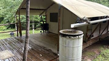 A tent with a wooden deck, a metal barrel, and a small orange bucket.