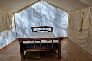 A tented room with a wooden bed, a window, and a view of trees.