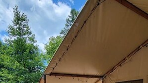 Una terraza de madera con una mesa de picnic y bancos, un espacio cubierto con sillas y una hamaca.