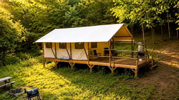 Una carpa con una terraza de madera, una parrilla y una mesa de picnic en un bosque.
