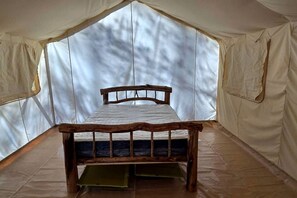A tented room with a wooden bed, a window, and a view of trees.