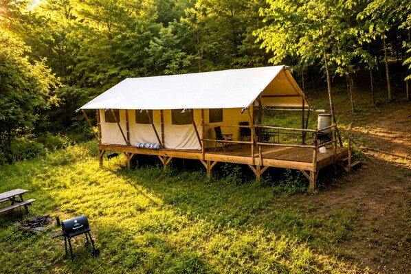 Una carpa con una terraza de madera, una parrilla y una mesa de picnic en un bosque.