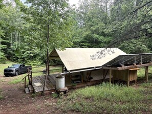 A rustic cabin with a large awning, a wooden deck, and a truck parked nearby.