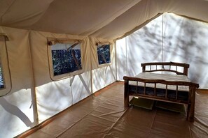 Una tienda de campaña con cama, ventanas y vistas al bosque.