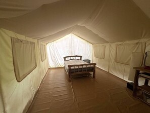 Una tienda de campaña con cama, una mesita y una ventana.