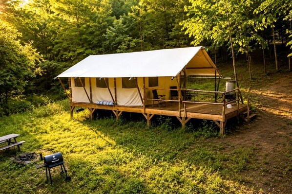 A tent with a wooden deck, a grill, and a picnic table in a forest.