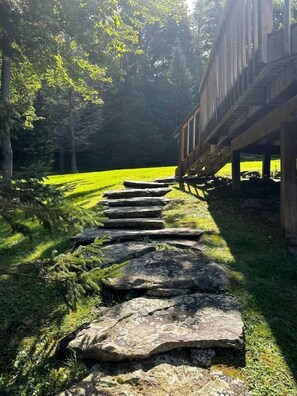 Un sendero de piedra que lleva a una estructura de madera rodeada de árboles y césped.