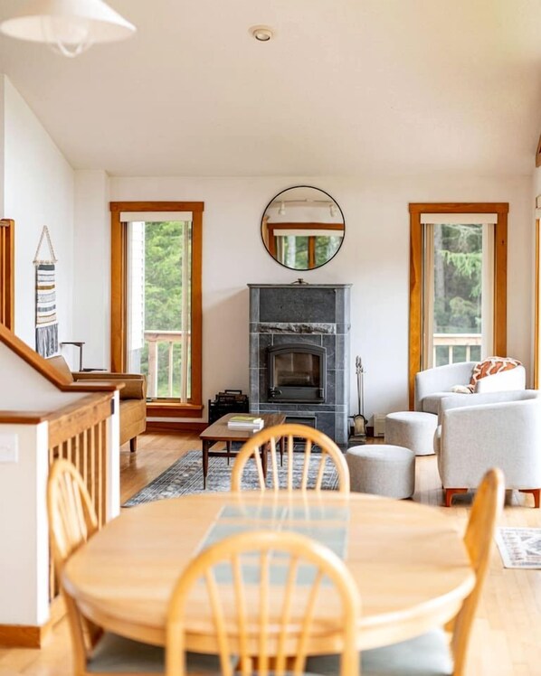 A spacious living room with a fireplace, large windows, and a dining area with wooden furniture.