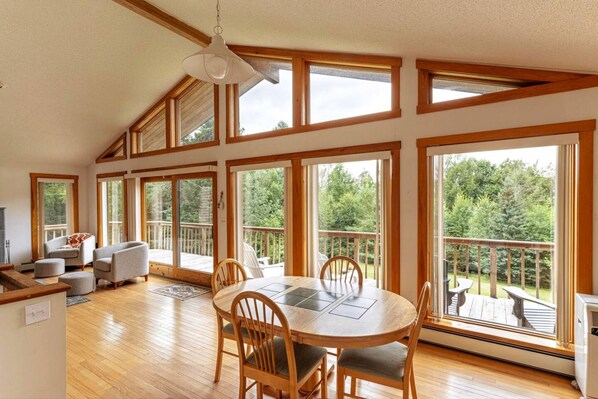Una habitación amplia con una gran mesa de comedor, varias sillas y vistas a una terraza y árboles.