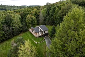 Una casa de dos pisos con terraza, rodeada de un bosque denso.