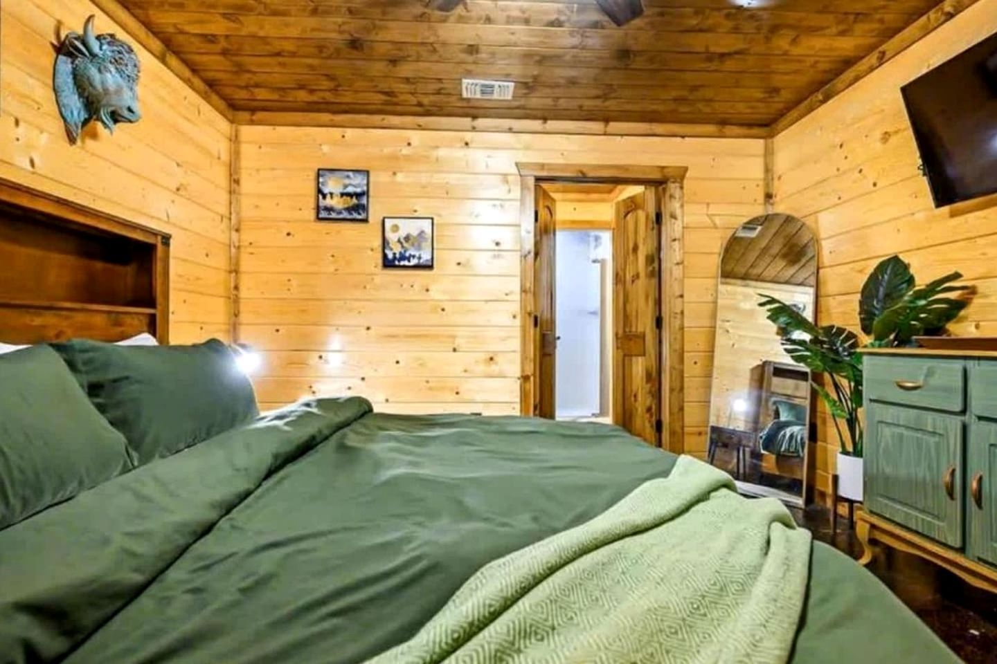 A wooden cabin bedroom with a bed, a dresser, and a wall-mounted TV.
