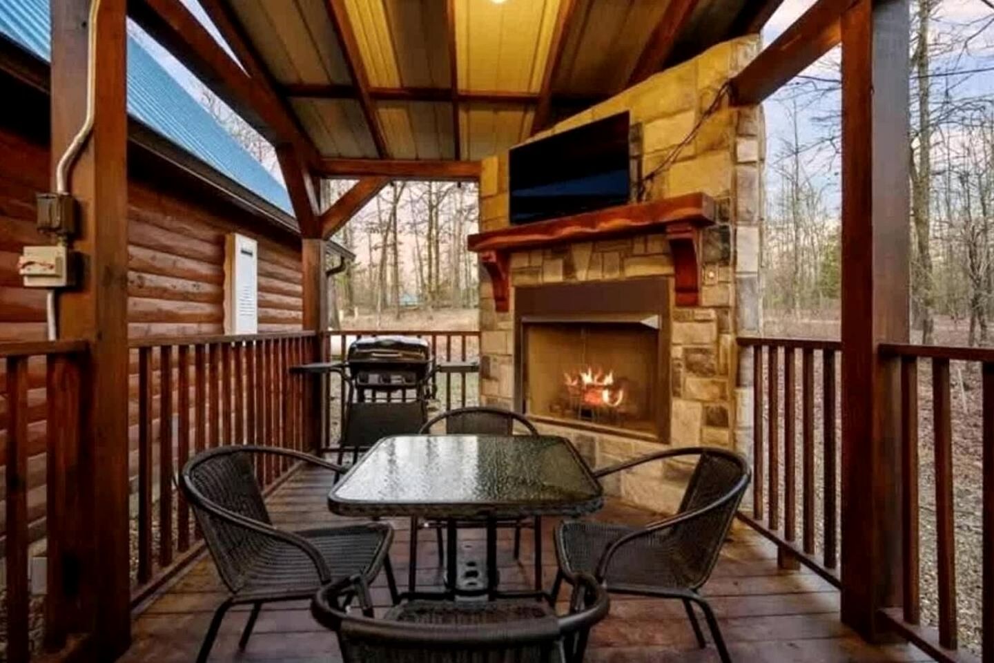 A wooden deck with a stone fireplace, a table, and chairs.