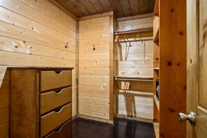 A wooden-paneled room with a wooden dresser, a hanging rack, and a door. - Luxury Pine Ridge Lodge with Hot Tub, Sauna & Game Room in Broken Bow, OK (Broken Bow)