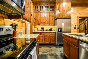 A kitchen with wooden cabinets, a stainless steel refrigerator, and a granite countertop. - Luxury Pine Ridge Lodge with Hot Tub, Sauna & Game Room in Broken Bow, OK (Broken Bow)