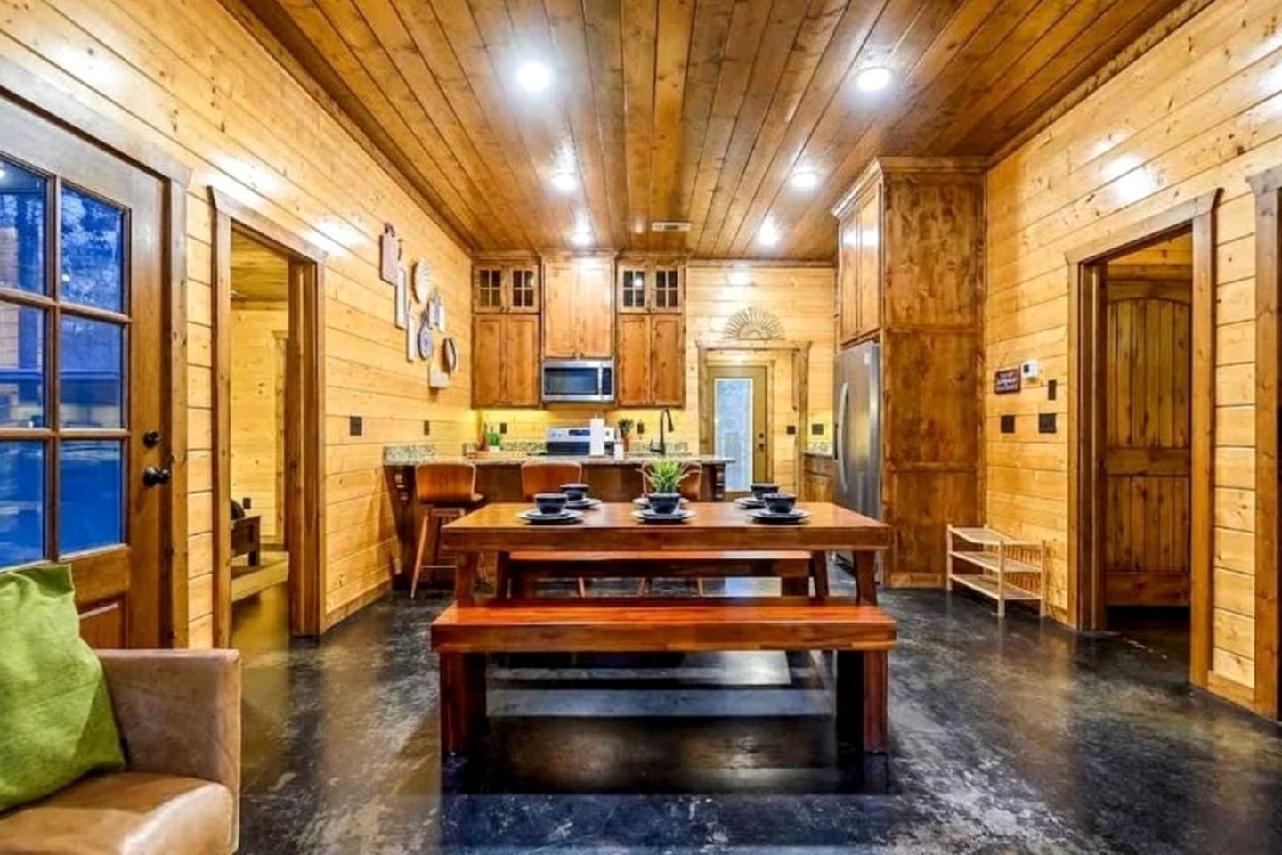Interior de una cabaña de madera con comedor, cocina y un ventanal grande.