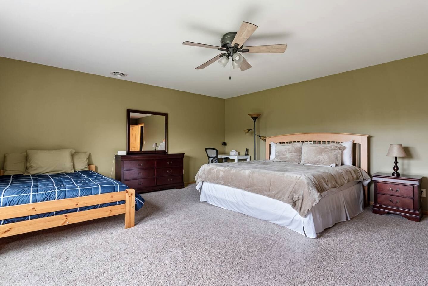 Une chambre à coucher comprenant un lit, une commode, un bureau, une chaise, une lampe et un ventilateur de plafond.