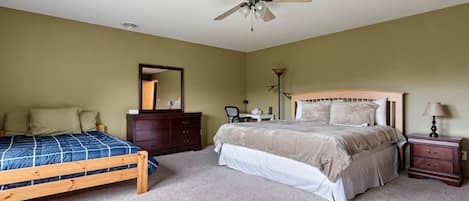 Un dormitorio con cama, cómoda, escritorio, silla, lámpara y ventilador de techo.