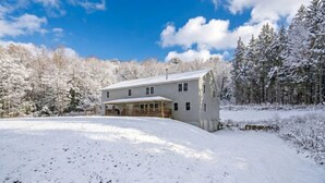 A two-story house with a covered porch, surrounded by snow-covered trees and a clear sky. - Peaceful Estate Designed for Connection & Relaxation in Andes, New York (Andes)