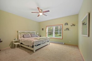 Ein Schlafzimmer mit Bett, Nachttisch, Deckenventilator, Fenster und Spiegel.