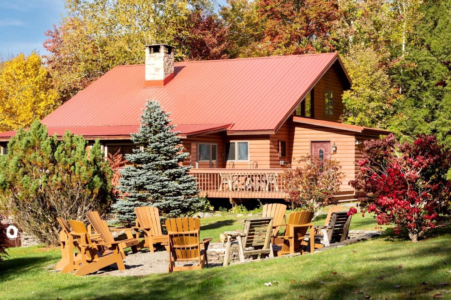 Une cabane en rondins avec un toit rouge, une terrasse et des meubles de jardin.