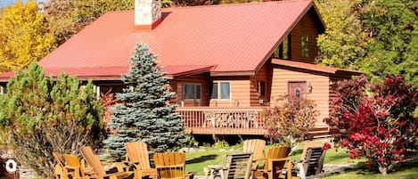 Une cabane en rondins avec un toit rouge, une terrasse et des meubles de jardin.