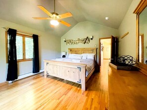 Ein Schlafzimmer mit einem hölzernen Bett, einem Deckenventilator, einem Fenster mit Vorhängen und einem an der Wand befestigten Kunstwerk.