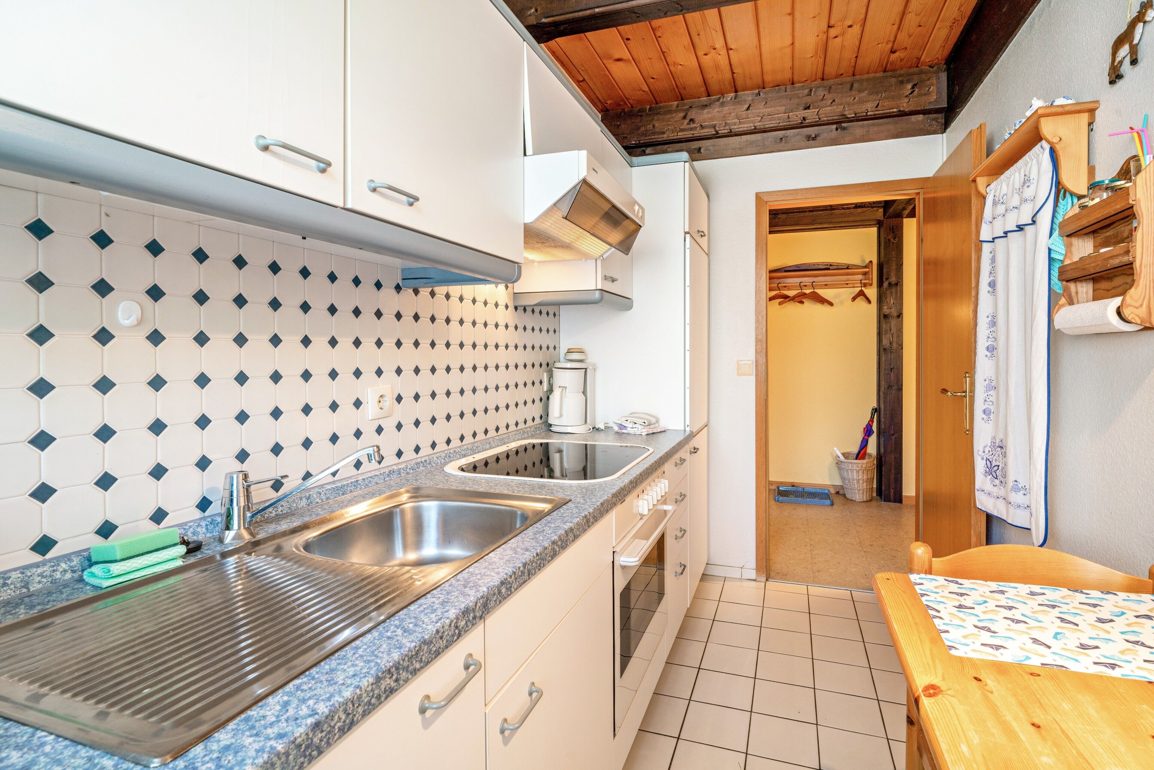 Eine Küche mit doppeltem Spülbecken, weißen Schränken, einer gefliesten Spritzschutzwand und einer Holzbalkendecke.