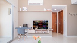 A modern living room with a flat-screen TV, a desk, a chair, and a potted plant.