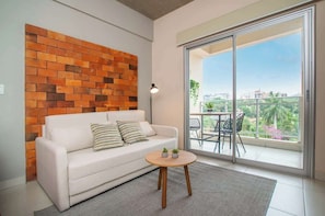 Ein modernes Wohnzimmer mit einem weißen Sofa, einer Ziegelwand, einem runden Holztisch und einem Balkon mit Blick.