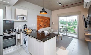 A compact kitchen with a central island, a washing machine, a microwave, and a dining area with a view. - Corporate Stays Bohemia (Asunción)