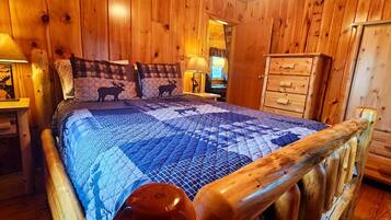 Une chambre dans un chalet en bois, avec un lit, une commode et une table de chevet dotée d’une lampe.